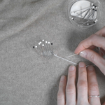Person sewing on cashmere with a small container of pins nearby.
