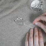 Person sewing on cashmere with a small container of pins nearby.
